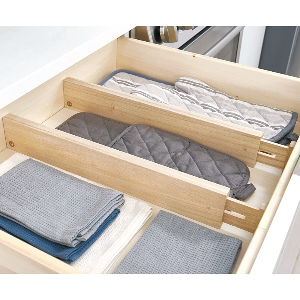 Eine Küchenschublade mit iDesign ECO - Schubladenteiler WOOD niedrig (Set 2 Stk.), die in getrennten Fächern graue und beige Topflappen und gefaltete Geschirrtücher übersichtlich organisiert.