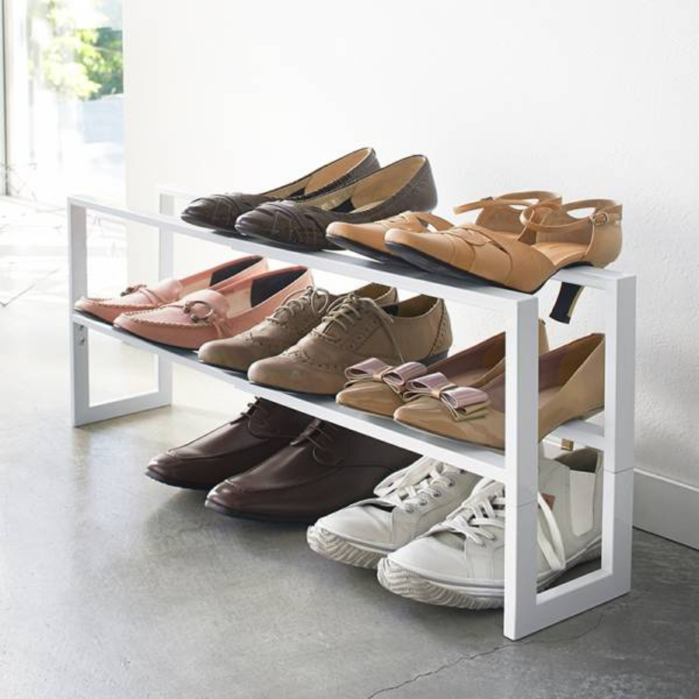 Das YAMAZAKI LINE Schuhregal ausziehbar - Weiss, ein weißes, zweistöckiges Regal, bewahrt in einem modernen Raum mit Betonboden sechs Paar Damenschuhe - Flats, Loafers, Lace-ups und Sneakers - stilvoll auf.