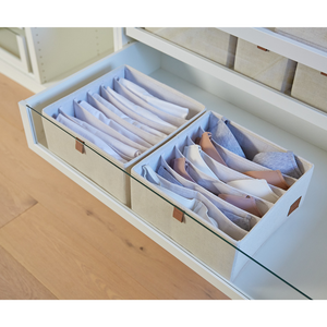 Zwei beigefarbene Love it Store it PREMIUM Organizer 6 Fächer breit (2er-Set) halten Hemden ordentlich gefaltet in einer weißen Schrankschublade mit Glasfront. Holzboden und zusätzliche Aufbewahrungsboxen sind oberhalb des Schrankes sichtbar.