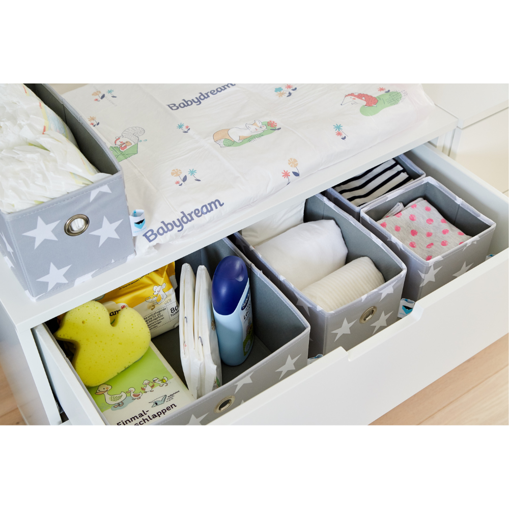 Eine geordnete Wickelkommode mit dem Love it Store it STAR Organizer Grau - Set 5 Stk. zur ordentlichen Aufbewahrung von Windeln, Feuchttüchern, Lotion, einem gelben Schwamm, Babykleidung und Tüchern unter einer spielerisch illustrierten Wickelunterlage in sternförmig angeordneten Boxen.