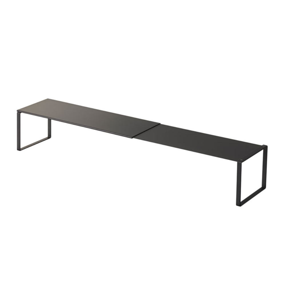 Das YAMAZAKI FRAME Schuhregal ausziehbar in Schwarz ist ein minimalistisches, schwarzes Metallregal mit einer rechteckigen Oberfläche und offenen, rechteckigen Beinen an beiden Enden, die zusätzlichen Stauraum für Ihre Utensilien bieten. Abgebildet auf einem weißen Hintergrund.