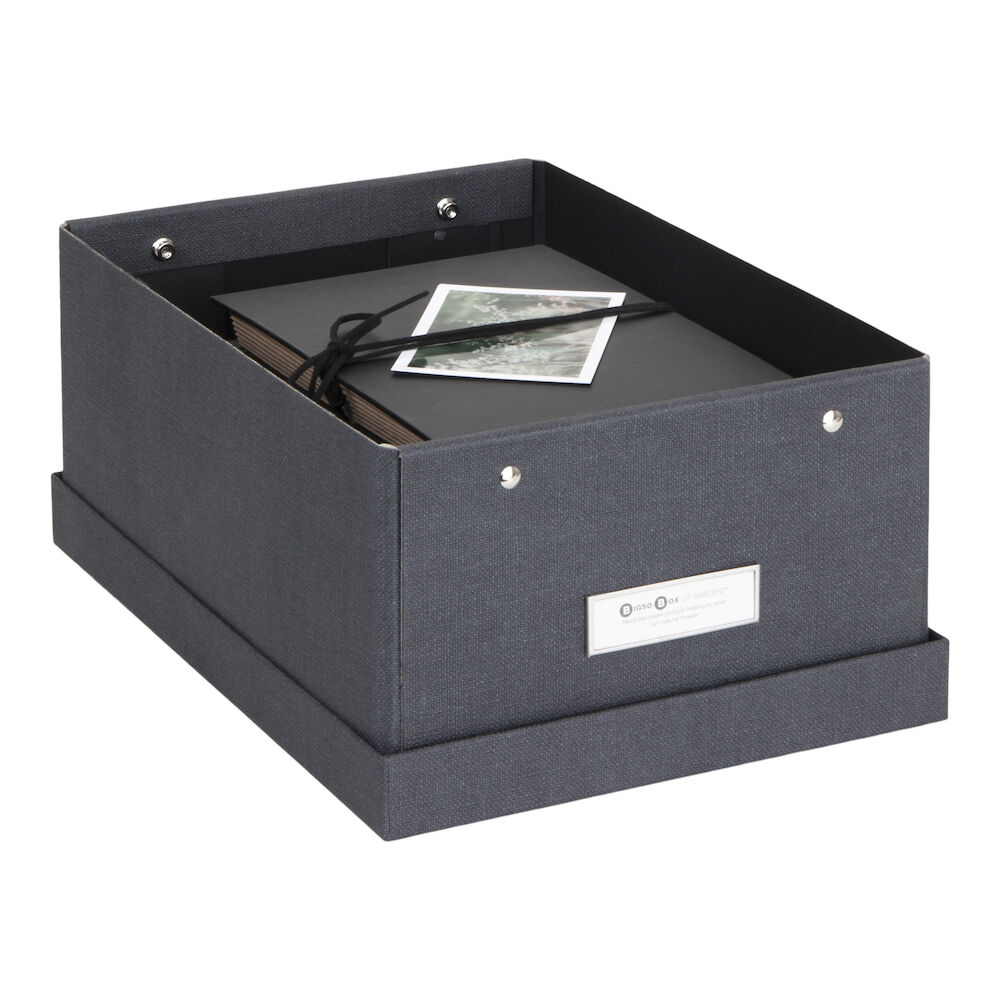 Die Bigso KARIN Aufbewahrungsbox aus schwarzem Segeltuch hat Metallnieten und einen Etikettenhalter auf der Vorderseite. Im Inneren finden Sie ein schwarzes Fotoalbum und zwei lose Fotos. Die Box ist stapelbar für einfaches Stapeln.