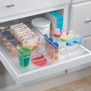 In einer aufgeräumten Küchenschublade steht das iDesign Küchen-Set MINI (5-teilig) mit klaren, stapelbaren Ordnungssystemen für Babynahrung, Snacks, Beutel und Flaschen mit farbigen Verschlüssen. Weiße Schubladen und Schränke unterstreichen den organisierten Look.