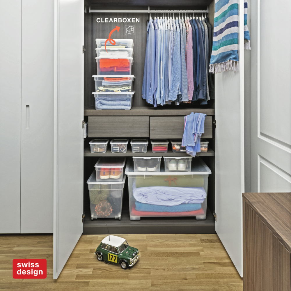 Kleiderschrank mit gestapelten Clearboxen, bekleidet, neben laufendem Modellauto auf Holzboden.