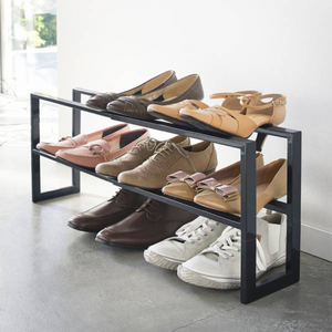 Schuhregal mit verschiedenen Schuhen, steht auf Betonboden neben einer weißen Wand.