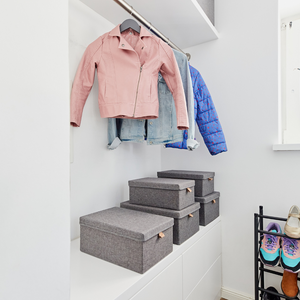Ein aufgeräumter Kleiderschrank mit rosa Jacke, Jeanshemd und blauer Jacke hängt über dem Love it Store it PREMIUM Aufbewahrungsboxen mit Deckel Grau - Set 5 Stk. Schuhe und Turnschuhe sind ordentlich auf einem schwarzen Schuhregal auf der rechten Seite angeordnet - perfekt für Ordnung Zuhause.
