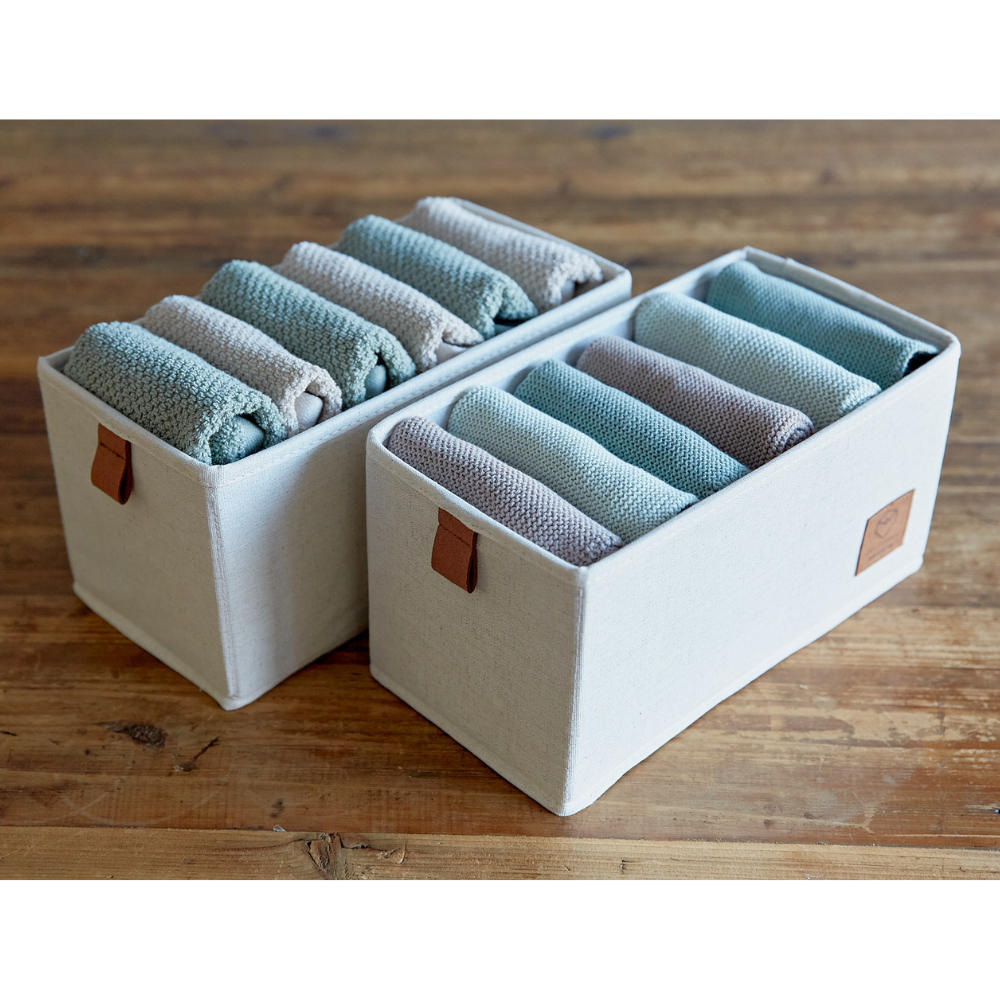 Zwei PREMIUM Organizer 6 Fächer schmal Beige - Set 2 Stk von Love it Store it, gefüllt mit fein säuberlich aufgerollten blauen und grauen Handtüchern, stehen auf einer Holzfläche. Jeder Aufbewahrungsbehälter hat ein braunes lederähnliches Etikett für einen stilvollen Touch.