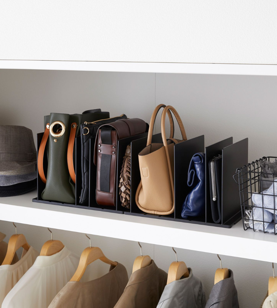 Mehrere Handtaschen und Clutches sind in zwei YAMAZAKI TOWER Taschen-Organizer Schwarz (Set 2 Stk.) mit verstellbaren Trennwänden auf einem weißen Schrankregal aufgeräumt, neben Hüten und gefalteter Kleidung. Darunter hängen Hemden.