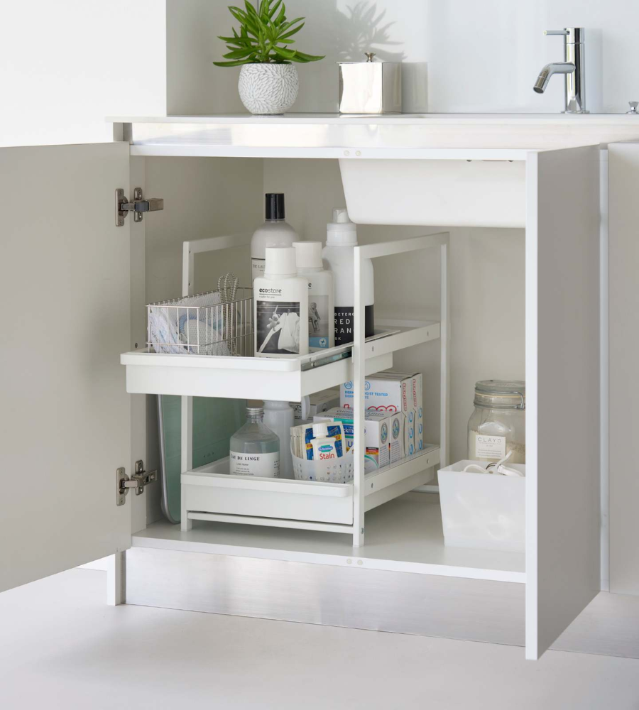 Im offenen Badezimmerschrank unter dem Waschbecken sind Flaschen, Lotionen und Reinigungsmittel auf einem YAMAZAKI TOWER Schubladenregal 2-stöckig - Weiss geordnet. Eine kleine Pflanze schmückt den Tresen darüber.