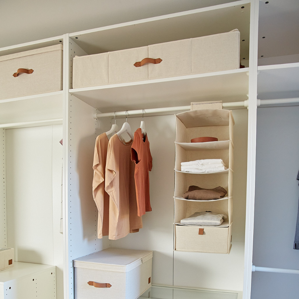 Offener Kleiderschrank mit beigen Aufbewahrungsboxen, drei pfirsichfarbenen und beigen Hemden auf Bügeln und einem Hängeorganizer. Die PREMIUM Aufbewahrungsbox Beige - Unterbett-Lagerung von Love it Store it sorgt für Ordnung - perfekt für IKEA PAX Kleiderschränke in neutralen Tönen.