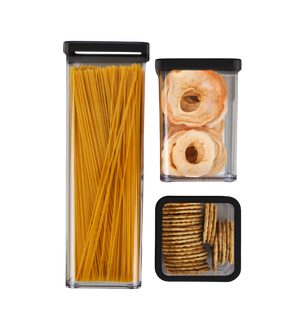 Drei transparente Behälter mit schwarzen Deckeln enthalten Spaghetti, Apfelringe und Cracker auf neutralem Hintergrund.
