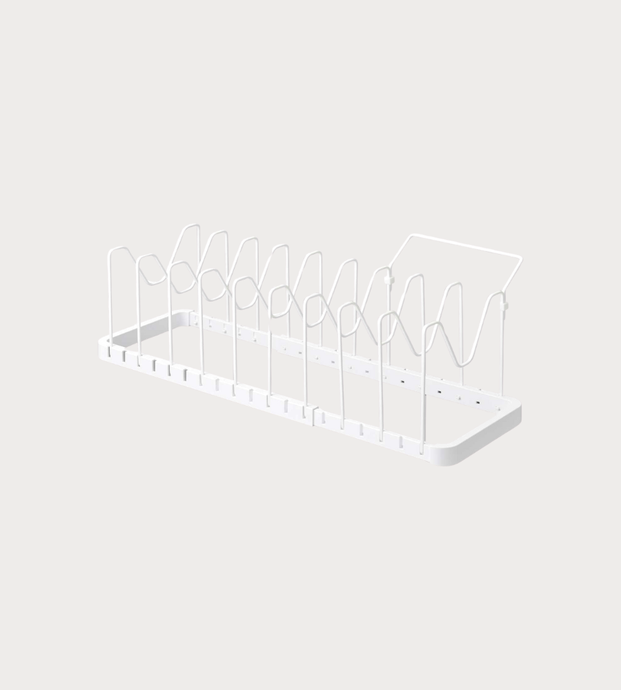 Der YAMAZAKI TOWER Kochgeschirr-Organizer ausziehbar in Weiß ist ein minimalistisches Metall-Dish-Rack mit vertikalen Teilern und flachem Boden - ideal zum Organisieren von Tellern und Schneidebrettern. Der Hintergrund ist schlicht und hell.