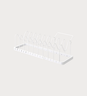 Der YAMAZAKI TOWER Kochgeschirr-Organizer ausziehbar in Weiß ist ein minimalistisches Metall-Dish-Rack mit vertikalen Teilern und flachem Boden - ideal zum Organisieren von Tellern und Schneidebrettern. Der Hintergrund ist schlicht und hell.