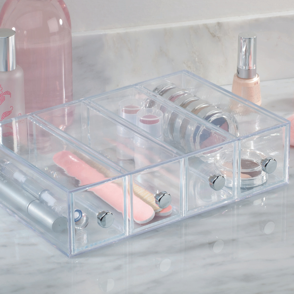 Der iDesign DRAWER Schubladen-Turm KLAR 4 Fächer - Schmal sorgt mit seinen stapelbaren Acryl-Schubladen für ordentliche Aufbewahrung von Kosmetik wie Nagelfeilen, Lippenstiften und Lidschatten auf der Marmor-Arbeitsplatte.