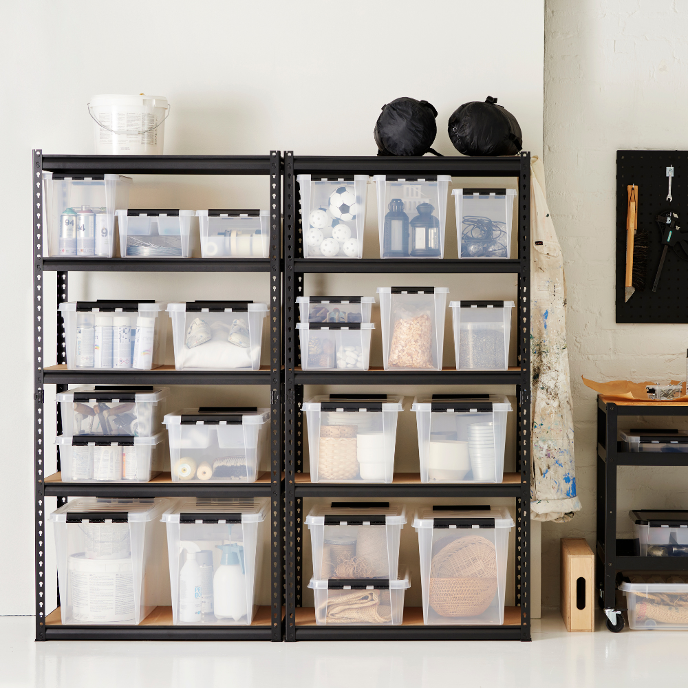Zwei schwarze Metallregale halten Orthex SmartStore Box KLAR 40x30x18cm (14L) Behälter gefüllt mit Haushalts- und Handwerksartikeln, neben einer Wand mit einer hängenden Schürze und Werkzeugen. Ein kleiner Rollwagen steht daneben.