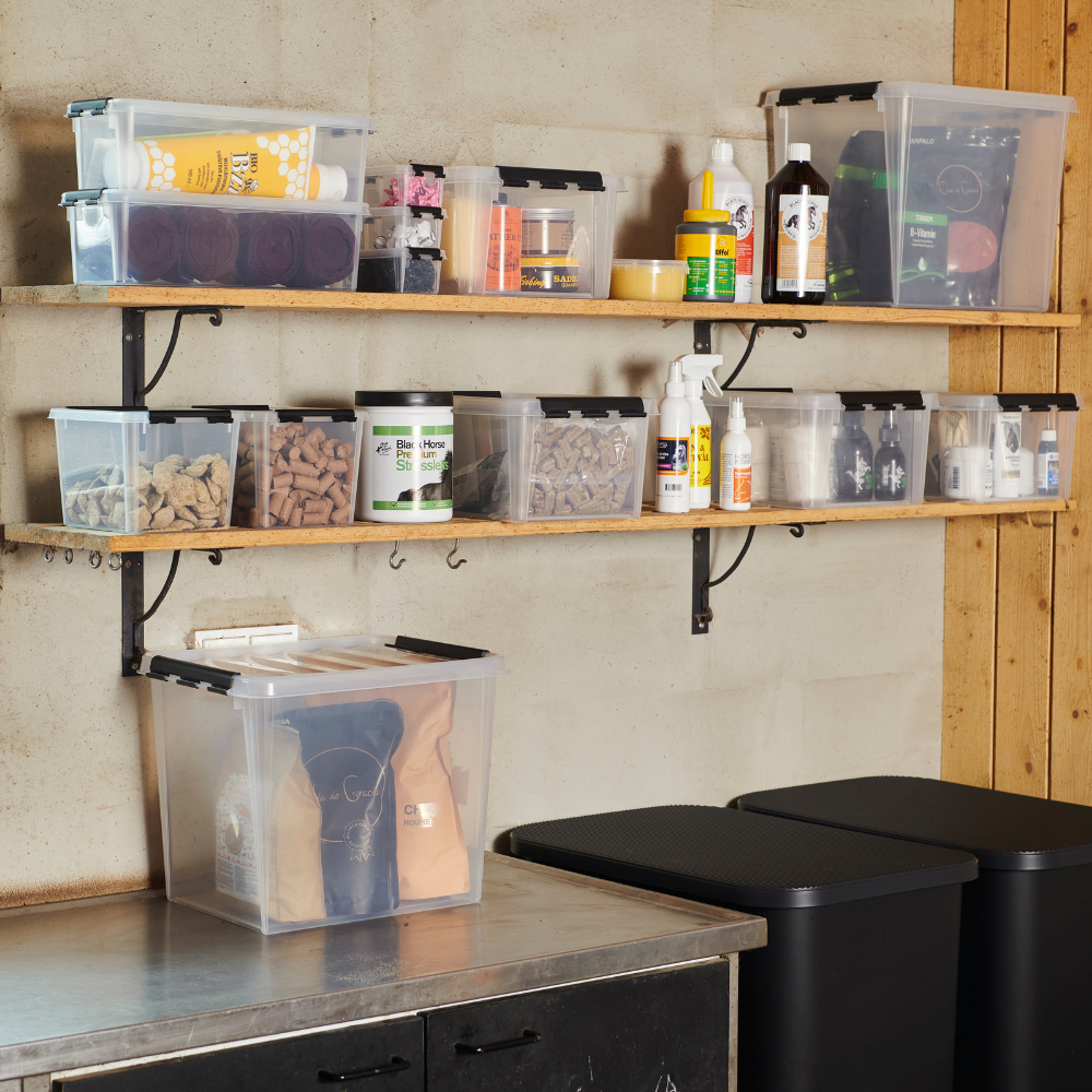 Zwei Holzböden nehmen Orthex SmartStore Box KLAR 40x30x18cm (14L) klare Behälter auf, die alle BPA-frei und stapelbar sind. Darunter bietet die Arbeitsplatte Platz für weitere Boxen, während rechts zwei schwarze Mülleimer stehen. Der Raum wirkt aufgeräumt und organisiert.