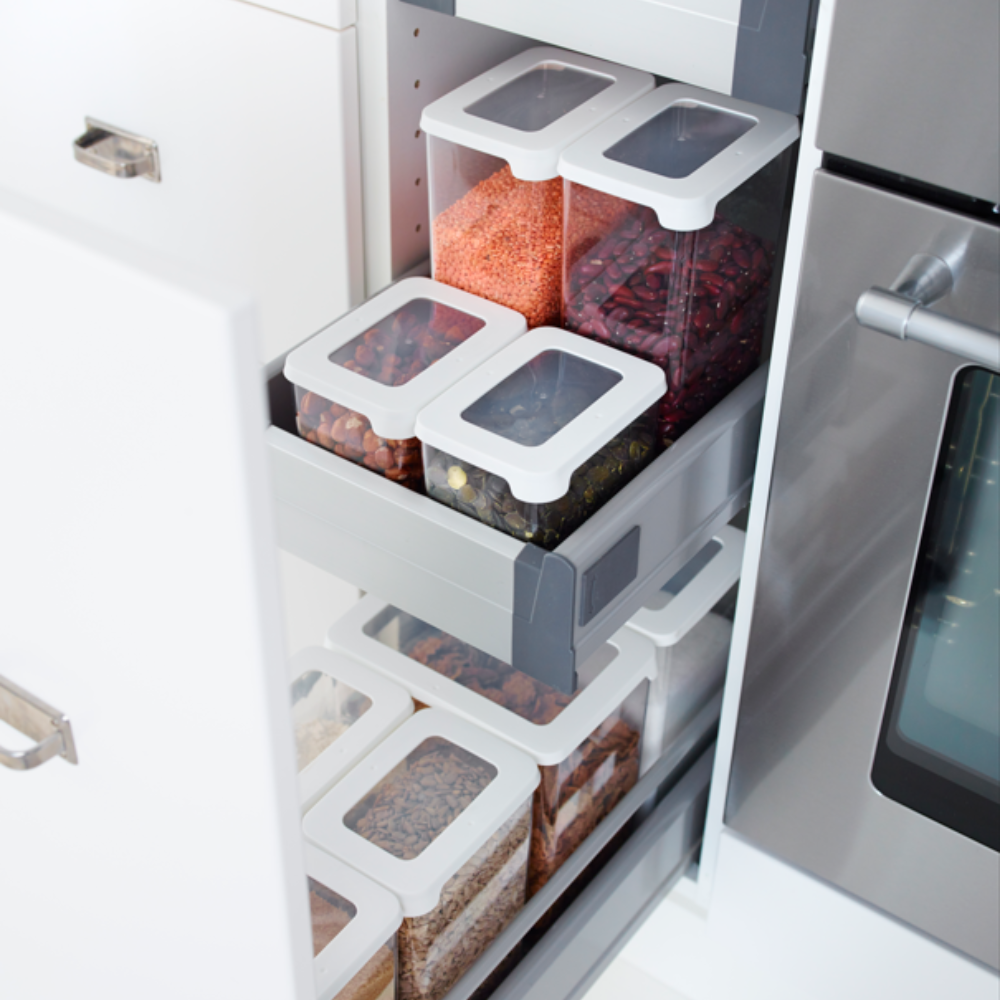 A set of Orthex SmartStore Clear-White storage containers—each airtight and filled with grains, lentils, beans, and pasta—is neatly arranged on pull-out shelves in a kitchen cabinet next to the oven.