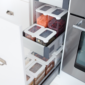 A set of Orthex SmartStore Clear-White storage containers—each airtight and filled with grains, lentils, beans, and pasta—is neatly arranged on pull-out shelves in a kitchen cabinet next to the oven.