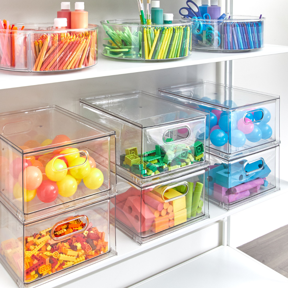 IDesign HOME EDIT - Aufbewahrungsbox Schublade KLAR (35x26,7x19,7cm) bewahrt Kunstzubehör und Spielzeug wie Stifte, Marker, Scheren, Bälle und Bauklötze nach Farben geordnet auf weißen Regalböden auf.