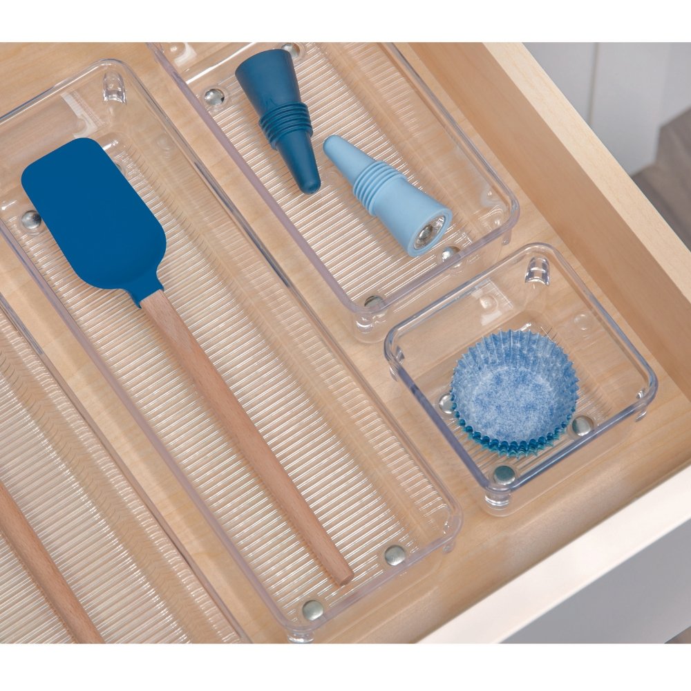Spatel und Trichter in transparenten Fächern einer Holzschublade, blaues Muffinförmchen im Vordergrund.