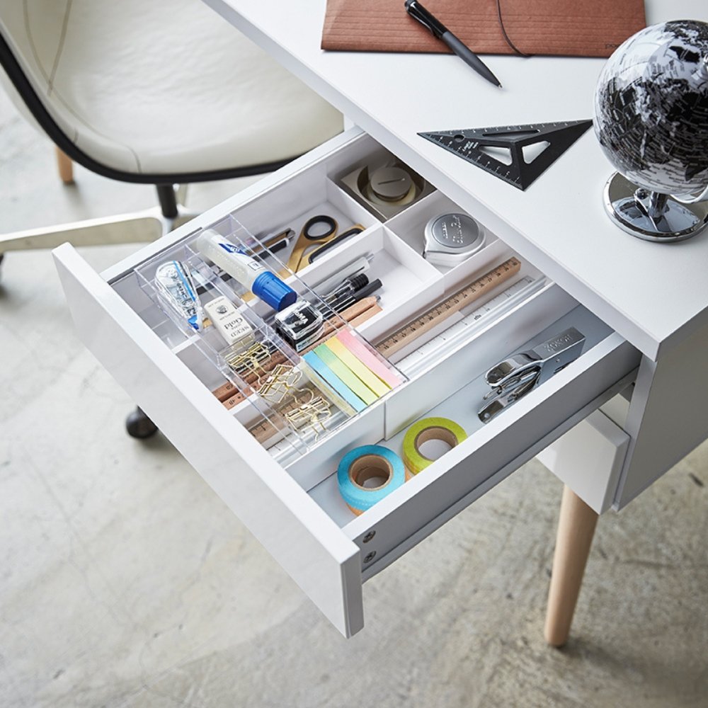 Schublade mit Büromaterial wie Stiften, Lineal und Klebeband, auf weißem Schreibtisch mit Globus.